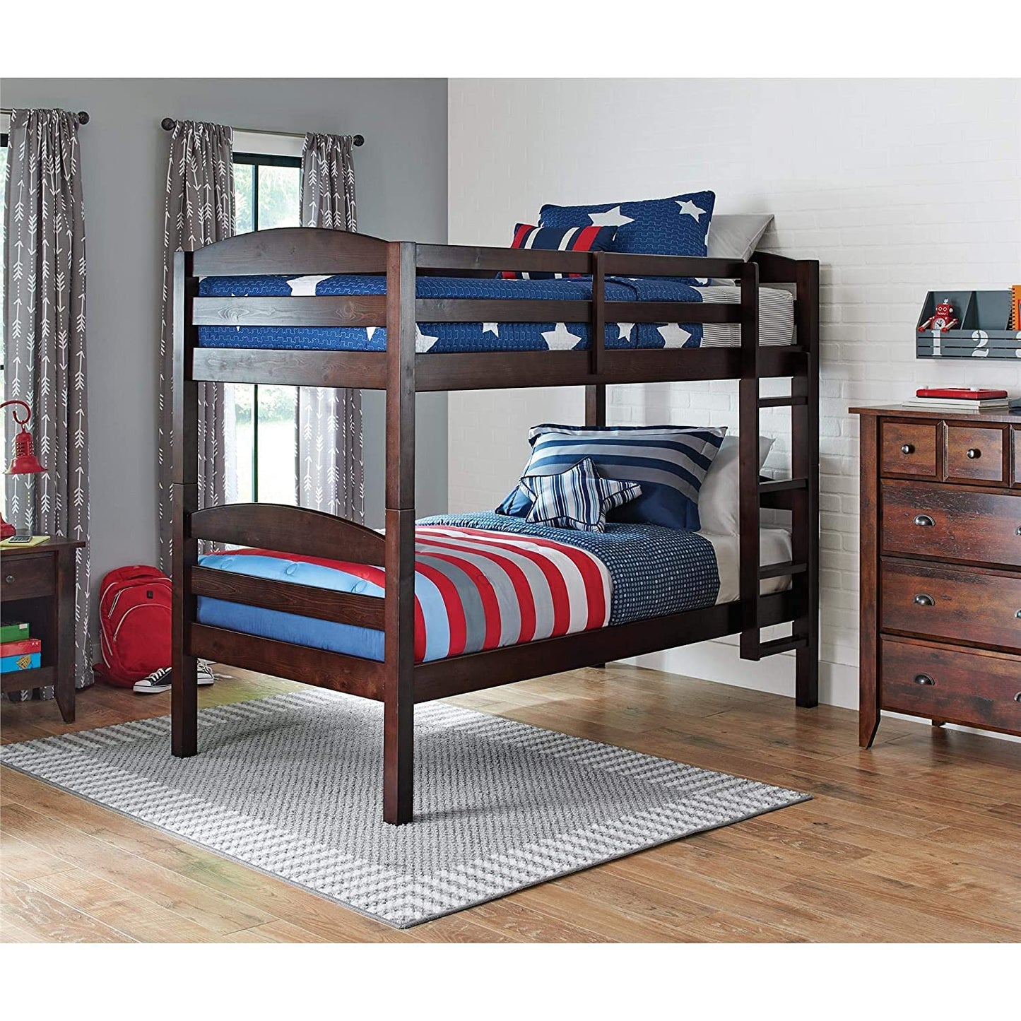 A brown wooden bunk bed with a ladder, featuring a lower bed with a blue mattress and a upper bed with a red and blue striped mattress. 
