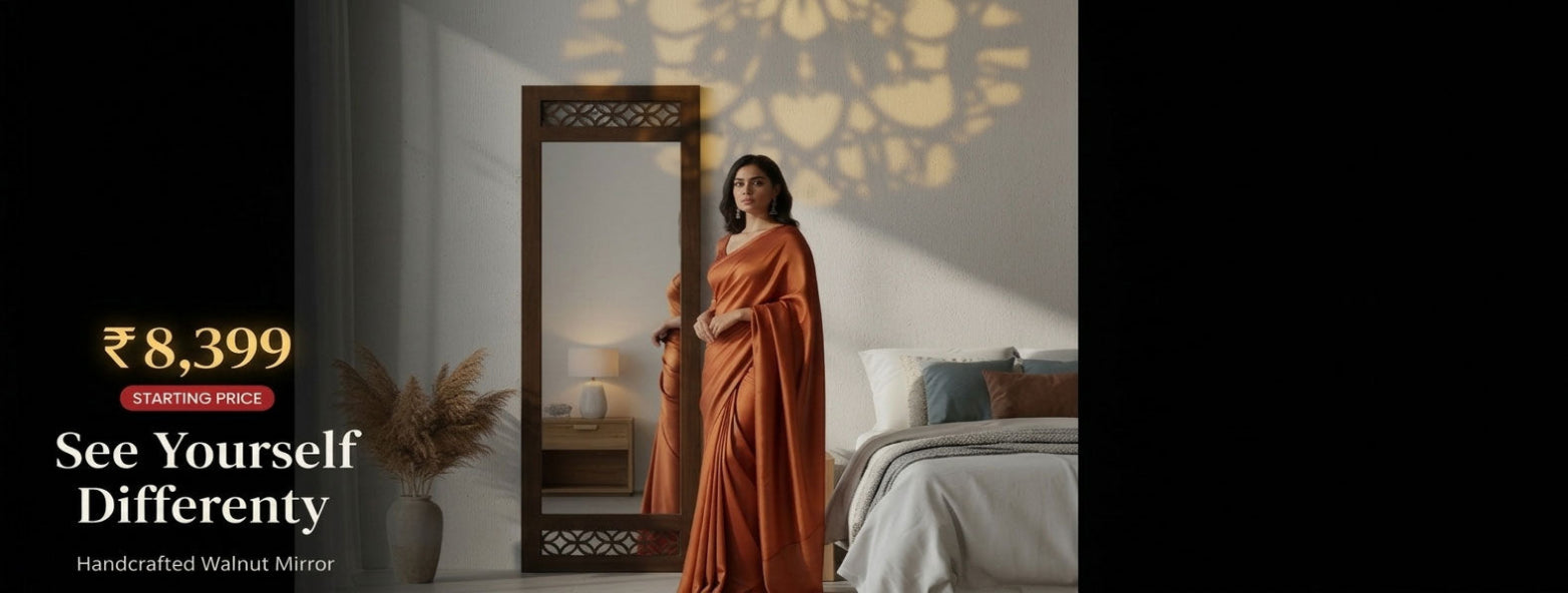 Woman in an orange saree standing next to a handcrafted walnut mirror in a bedroom setting.